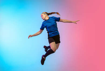 High jumping. Female soccer, football player training in action isolated on gradient studio background in neon light. Concept of motion, action, ahievements, healthy lifestyle. Youth culture.の写真素材