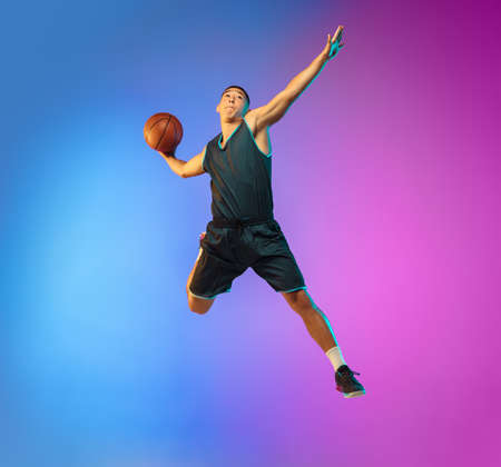 Winner. Young basketball player in action, motion in high jump on gradient background in neon. Concept of sport, movement, energy and dynamic, healthy lifestyle. Training, practicing, trendy colors.の写真素材