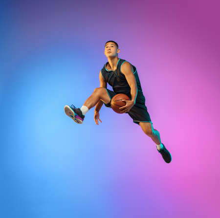 Winner. Young basketball player in action, motion in high jump on gradient background in neon. Concept of sport, movement, energy and dynamic, healthy lifestyle. Training, practicing, trendy colors.の写真素材