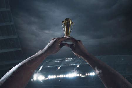 Hard work. Award of victory, male hands tightening the golden cup of winners against cloudy dark sky. Sport, competition, championship, winning, achieving the goal. Prize for success and honor.の写真素材
