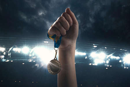 Champion. Award of victory, male hands tightening the golden medal of winners against cloudy dark sky. Sport, competition, championship, winning, achieving the goal. Prize for success and honor.の写真素材