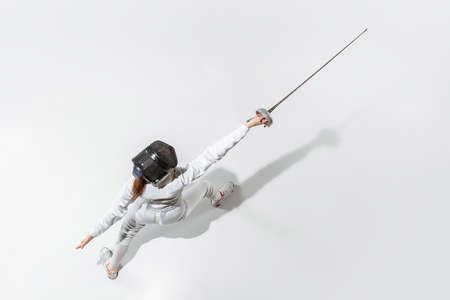 Champion. Teen girl in fencing costume with sword in hand on white background. Top view. Young female model practicing and training in motion, action. Copyspace. Sport, youth, healthy lifestyle.の写真素材