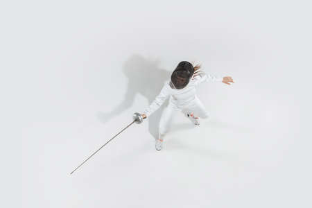 First. Teen girl in fencing costume with sword in hand on white background. Top view. Young female...