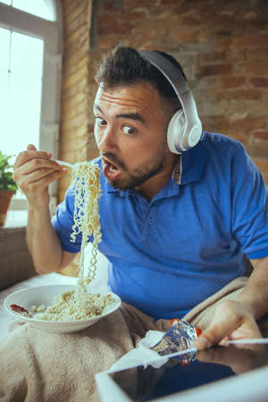 Eating instant noodle, watching match, championship, cinema. Lazy man living in his bed surrounded...