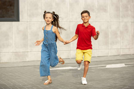 Two smiling kids, boy and girl running together in town, city in summer day. Concept of childhood,...