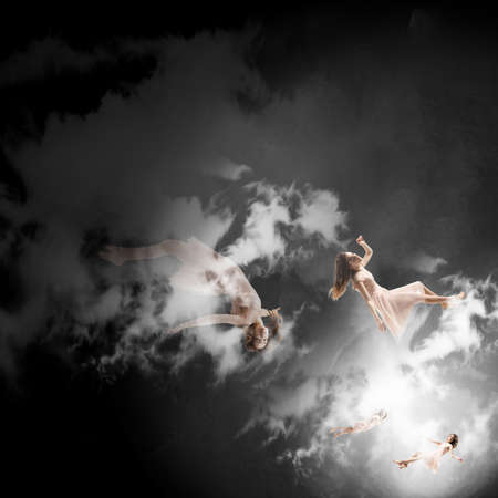 Mid-air beauty cought in clouds. Full length shot of attractive young woman hovering in air and keeping eyes closed. Levitating in free falling, lack of gravity. Freedom, emotions, artwork concept.の写真素材