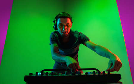 Fire. Young caucasian musician in headphones performing on bicolored pink-purple background in neon...