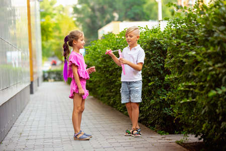 Sincere. Two smiling kids, boy and girl running together in town, city in summer day. Concept of childhood, happiness, sincere emotions, carefree lifestyle. Little caucasian models in bright clothes.の写真素材