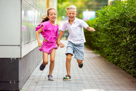 Friends. Two smiling kids, boy and girl running together in town, city in summer day. Concept of childhood, happiness, sincere emotions, carefree lifestyle. Little caucasian models in bright clothes.の写真素材