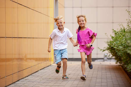 Future. Two smiling kids, boy and girl running together in town, city in summer day. Concept of childhood, happiness, sincere emotions, carefree lifestyle. Little caucasian models in bright clothes.の写真素材