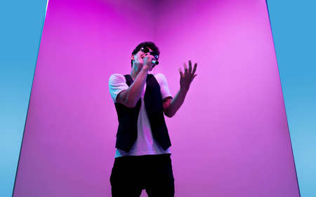 Talented. Young male musician, singer performing on pink-blue background in neon light. Concept of...
