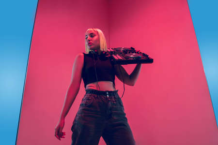 Hero. Young female stylish, fashionable musician performing on blue-red background in neon light. Concept of music, hobby, festival, entertainment, emotions. Joyful party host, DJ, portrait of artist.の写真素材