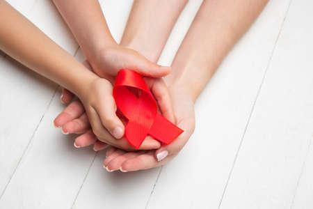 Female and male hands holding red HIV and AIDS awareness ribbon isolated on wooden background....