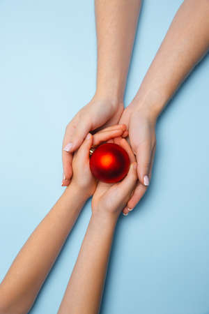 Humans hand holding a Christmas ball isolated on blue background. Concept of celebration, holidays, family, home comfort, winters holidays, New Year eve. Gift for happy times.の写真素材