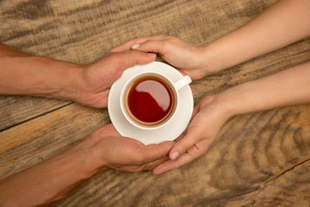 Hands of couple holding mug of tea, top view on wooden background with copyspace. Drinks, home comfort, warm event and evening, coziness with family. Copyspace for advertising.の写真素材