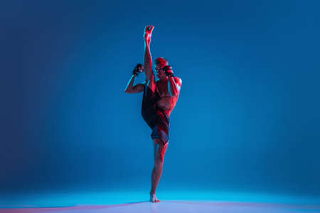 High flight. MMA. Professional fighter punching or boxing isolated on blue studio background in neon. Fit muscular caucasian athlete or boxer fighting. Sport, competition and human emotions, ad.の写真素材