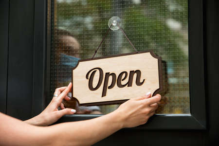 Open sign on the glass with reflection of street cafe or restaurant. Coronavirus pandemic new safety...