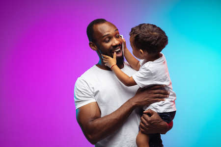 African-american father and son portrait on gradient studio background in neon. Beautiful male...