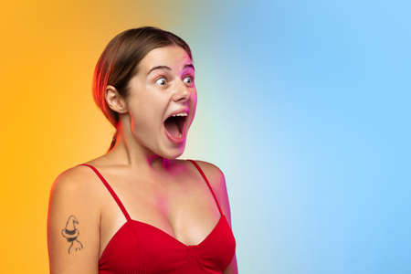 Astonished. Close up caucasian young womans portrait on gradient studio background in neon. Beautiful female model in casual style. Concept of human emotions, facial expression, youth, sales, ad.の写真素材