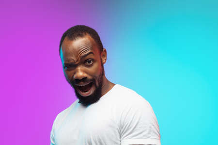 Playful, asking. African-american young mans portrait on gradient background in neon. Beautiful male...