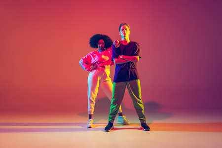 Summer. Stylish man and woman dancing hip-hop in bright clothes on green background at dance hall in neon light. Youth culture, movement, style and fashion, action. Fashionable portrait.の写真素材