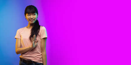 Greeting. Asian young womans portrait isolated on gradient studio background in neon. Beautiful...