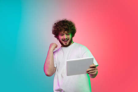 Winner. Caucasian young man portrait isolated on gradient studio background in neon light.の写真素材