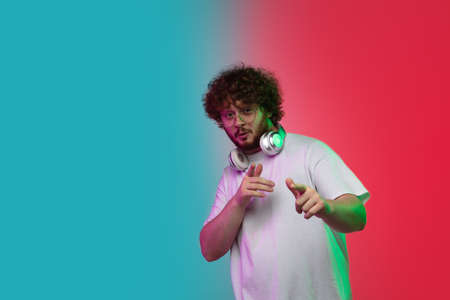 Pointing, showing. Caucasian young mans portrait on gradient studio background in neon light....