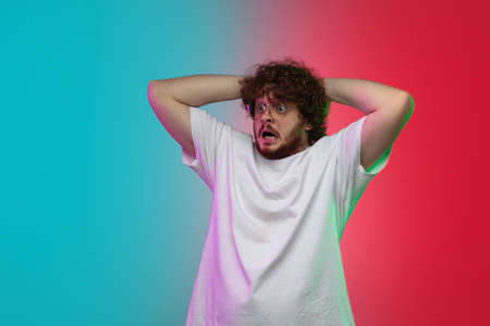 Crazy shocked. Caucasian young mans portrait isolated on gradient studio background in neon light....
