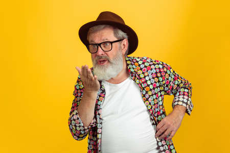 Sending kisses. Portrait of senior hipster man in eyewear isolated on yellow studio background. Tech...