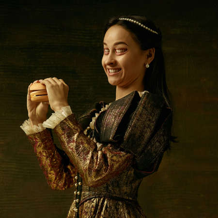 Medieval young woman in golden vintage clothing as a duchess posing on dark studio background....