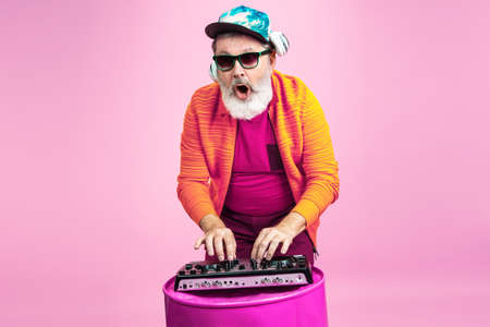 Party time. Portrait of senior hipster man in fashionable eyewear isolated on pink studio background. Tech and joyful elderly lifestyle concept. Trendy colors, forever youth. Copyspace for your ad.の写真素材