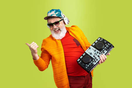 Party guy. Portrait of senior hipster man in fashionable eyewear isolated on green studio background. Tech and joyful elderly lifestyle concept. Trendy colors, forever youth. Copyspace for your ad.の写真素材