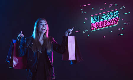 Online shopping. Portrait of young beautiful woman in neon light on dark studio backgound. Neoned lettering. Human emotions, black friday, cyber monday, purchases, sales, finance concept. Copyspace.の写真素材