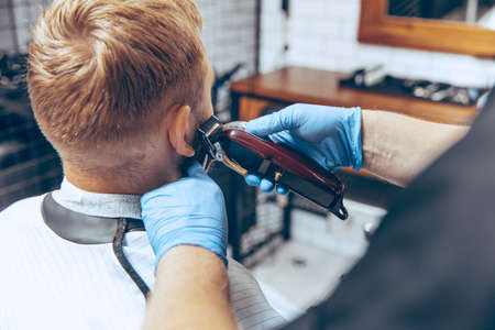 Close up man getting hair cut at the barbershop wearing mask during coronavirus pandemic. Professional barber wearing gloves. Covid-19, beauty, selfcare, style, healthcare and medicine concept.の写真素材