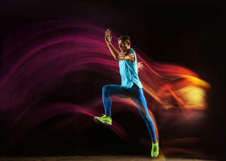 Professional male runner training isolated on black studio background in mixed light. Man in...