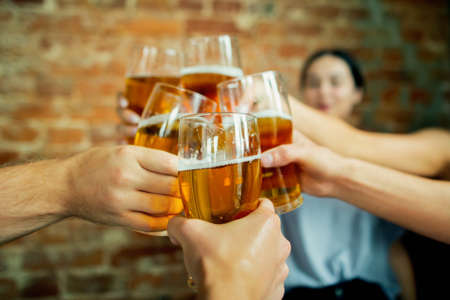 Close up clinking. Young group of friends drinking beer, having fun, laughting and celebrating together. Women and men with beers glasses. Oktoberfest, friendship, togetherness, happiness concept.の写真素材