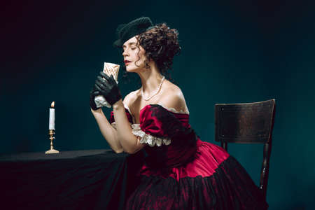 Eating fast food. Young woman as Anna Karenina isolated on dark blue background. Retro style,...