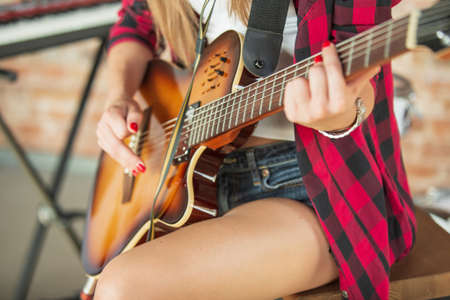 Close up, cropped. Beautiful woman in recording music, singing and playing guitar while sitting in loft workplace or at home. Concept of hobby, music, art and creation. Creating first single.の写真素材