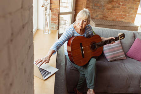 Learning to play guitar online. Senior woman studying at home, getting online courses,...