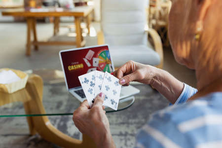 Playing poker, casino online. Senior woman studying at home, getting online courses, self-development. Caucasian woman using modern devices for education, spending time for new job or hobby, having fun.の写真素材