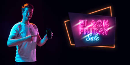 Selfie, astonished. Portrait of young man in neon on dark studio backgound. Human emotions, black friday, cyber monday, purchases, sales, finance concept. Copyspace.の写真素材