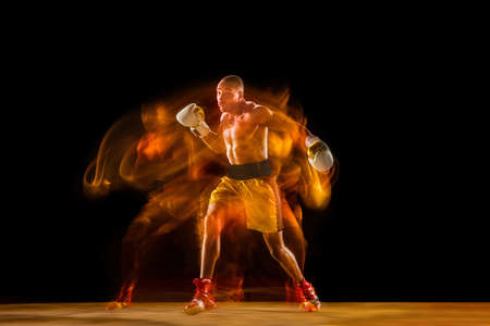 In fire. Professional boxer training isolated on black studio background in mixed light. Man in...