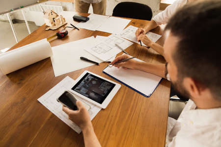 Close up hands of architect-engineer and young couple during presentation of future house. Top view table with documents, blueprint. First home, industrial, building concept. Moving to new live place.の写真素材