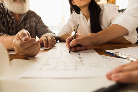 Close up hands of architect-engineer and young couple during presentation of future house. Top view...