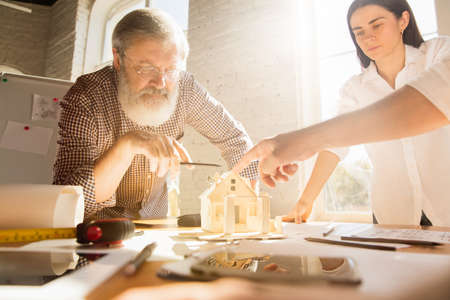 Hands of architect-engineer and young couple during presentation of future house. Side view table with documents, blueprint. First home, industrial, building concept. Moving to new live place.の写真素材
