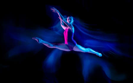 Ghost. Young and graceful ballet dancer on black studio background in neon mixed light. Art, motion, action, flexibility, inspiration concept. Flexible caucasian ballet dancer, weightless jumps.の写真素材