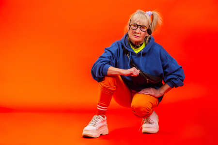 Styled up. Senior woman in ultra trendy attire isolated on bright orange background. Looks stylish and fashionable, forever young. Caucasian model in sunglasses, bright attire and sneakers.の写真素材