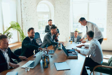 Playing poker, gambling on workplace. Happy carefree colleagues having fun in office while their co-workers working hard and highly concentrated. Concept of fun, resting, professional occupation.の写真素材