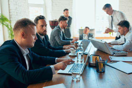 Playing poker, gambling on workplace. Happy carefree colleagues having fun in office while their co-workers working hard and highly concentrated. Concept of fun, resting, professional occupation.の写真素材